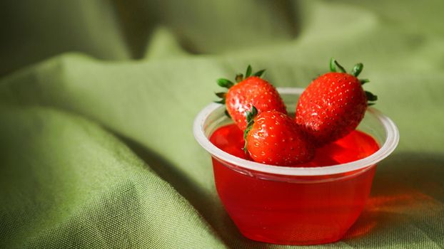 Red strawberry jelly with berries in a plastic container