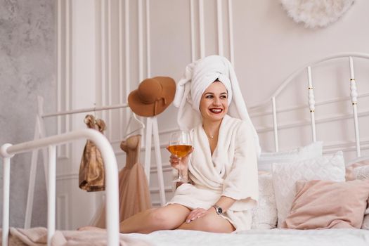 Beautiful woman in a white robe and with a towel on her hair with glass of wine