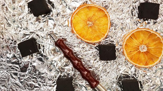 Coals for hookah on foil background with dry oranges