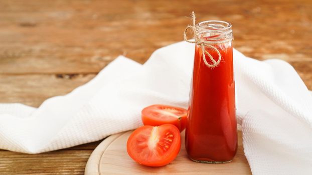 Tomato juice in glass bottle and fresh tomatoes on wooden background