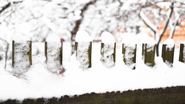 Wooden fence gate covered in white snow at heavy snowing snowstorm