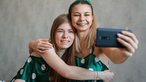 Beautiful happy girlfriends taking selfie with smartphone at pajama party