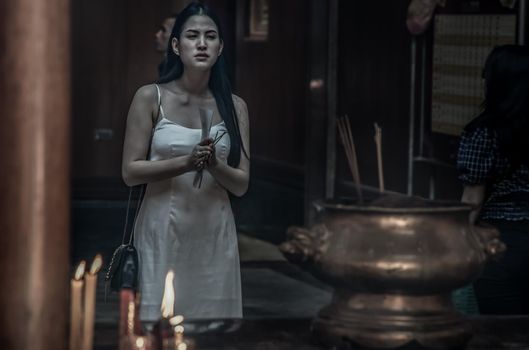 Beauty young woman in white dress Hold incense pray homage to buddha's blessing Within the Chinese shrine.