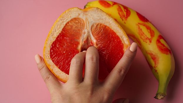 Fingers in grapefruit on pink background. Sex concept.