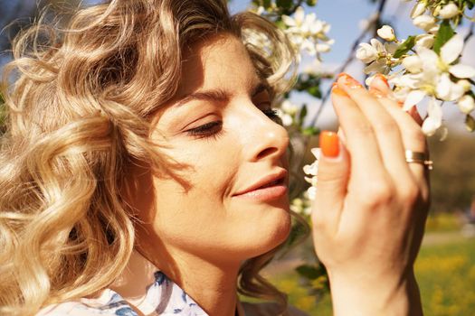Close-up of female face, woman sniffing white flowers blooming Apple tree