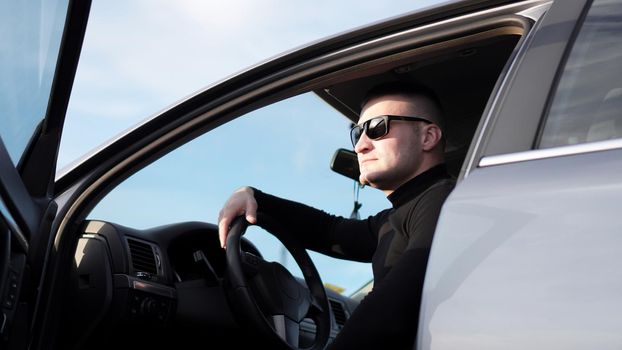Side view of confident young stylish man in sunglasses in his car