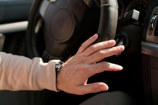 A man's hand on a steering wheel. Shabby steering wheel trim in a car.
