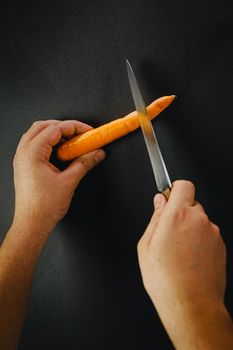 Two hands cutting a carrot with a long knife