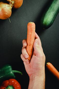 Hand grabbing a carrot surrounded by vegetables with a black table