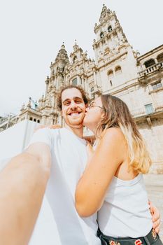 Young couple kissing in front of a cathedral during a sunny day