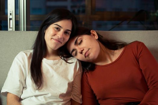 A lesbian couple on the couch smiling to camera on a modern flat