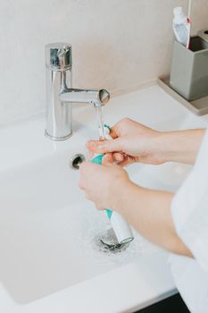 A woman washing his electrical toothbrush pieces with water after brushing his teeth