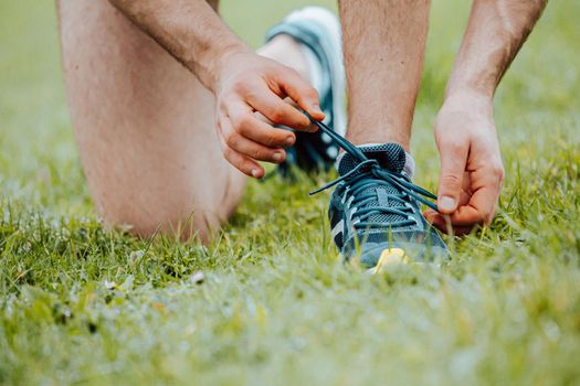 A super close up of a man tying the shoelaces on this sport shoes over green grass before training fitness