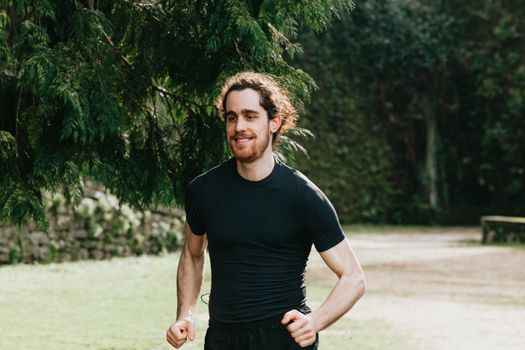 A close up of a long hair male running between the trees during a sunny day in the park