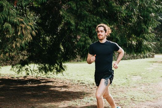 A long hair male running between the trees during a sunny day in the park with copy space