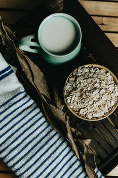 Cup of oat milk with oat seed on a bowl over a wooden plank