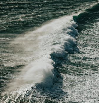 Aerial view of a massive wave crashing in the middle of the ocean