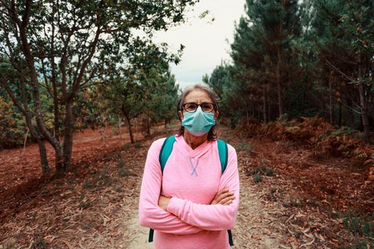 Frontal portrait of an old woman wearing a mask and sport clothes in the forest during a trekking day