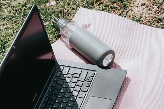 Close up of a laptop and a bottle of water over a yoga mat with the sun reflecting