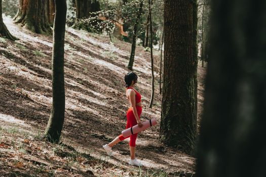 Young woman in fitness clothes walking in the middle of the forest holding a yoga mat