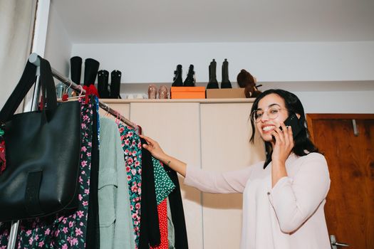 Woman smiling to camera selecting clothes to sell while using his phone, market and retail concepts