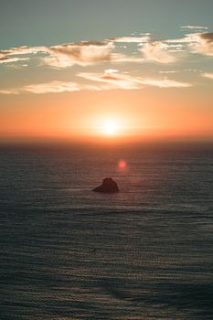 A massive sunset with sun flares over the ocean with a rock in the middle of the sea