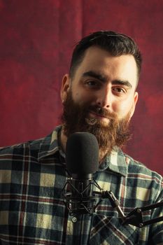 Young hipster man near a streaming microphone smiling with a red background and copy space
