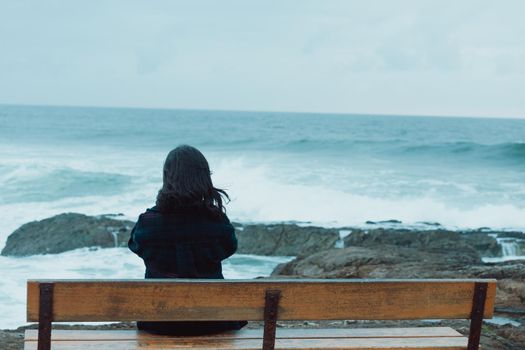 Woman giving the back to the camera sitting in a bench in front of a massive ocean with copy space