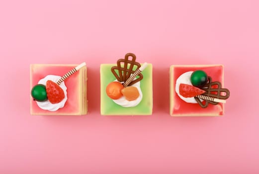 Top view of three colorful mini cakes on bright pink background