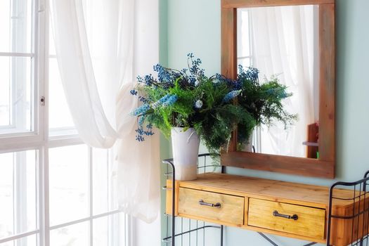 Elegant mirror in wooden frame above console table with flowers in vase in rustic bedroom interior near the window