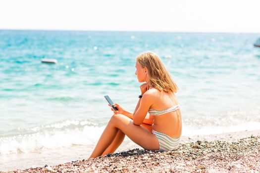 Teenage girl playing games and searching web on the telephone. Gadget dependency disorder problem for kids during holiday vacation at the seaside