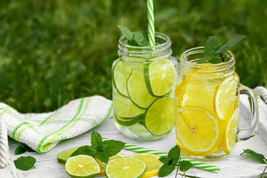 Cold refreshing homemade lemonade with mint, lemon and lime in mason jars on a summer lawn, copyspace
