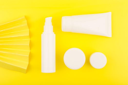 Top view of cosmetic products for skin care in white unbranded tubes on yellow background decorated with waver