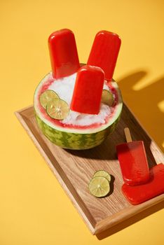 Watermelon popsicle on wood tray over yellow background