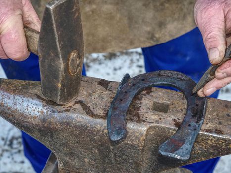 Blacksmith forging nail holes on horseshoe.