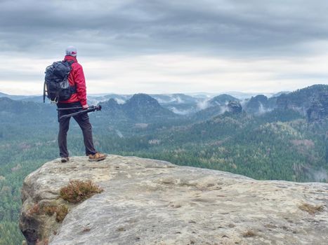 Alone hiker in warm red  jacket stand on peak of sandstone rock 