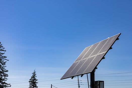 A free standing array of solar panels is pointed up at a clear blue sky. Power lines can be seen behind it in the background.
