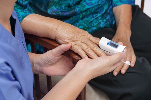 Caregiver monitoring oxygen saturation at fingertip of elderly woman.