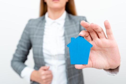 A Lady Holding Home In Business Outfit Presenting Possibility Of Owning Your Own Real Estate. Buying House Or Moving New Insurance Or Mortage Concept Shown By The Young Businesswoman.