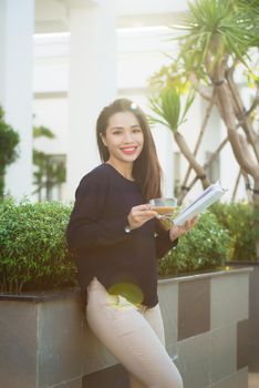 Happy young woman holding book fond of literature analyzing novel during leisure time on terrace of campus cafe in sunny day.