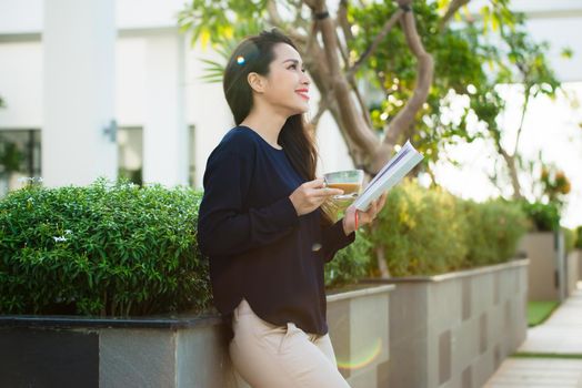Happy young woman holding book fond of literature analyzing novel during leisure time on terrace of campus cafe in sunny day.