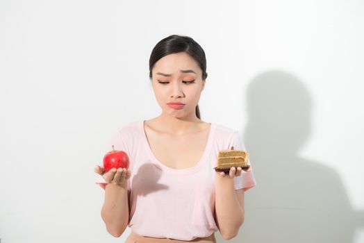 Woman holds in hand cake sweet and apple fruit choosing, trying to resist temptation, make the right dietary choice. Weight loss diet dilemma gluttony concept.