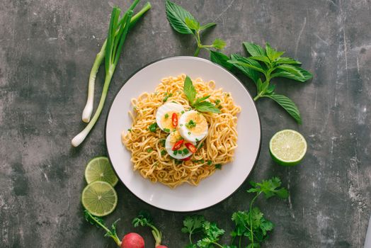 Dry instant noodles put egg with fresh herbs, garnish of cilantro and Asian basil, lemon, lime on dark stone background