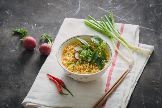 Instant noodles in bowl with radish, herbs and onion