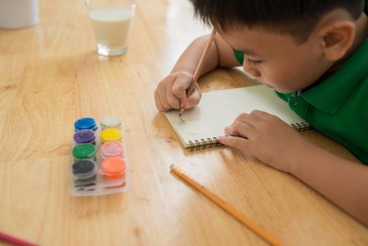 Cute boy doing homework, coloring pages, writing and painting. Children paint. Kids draw. Preschooler with books at home. Preschoolers learn to write and read. Creative boy.