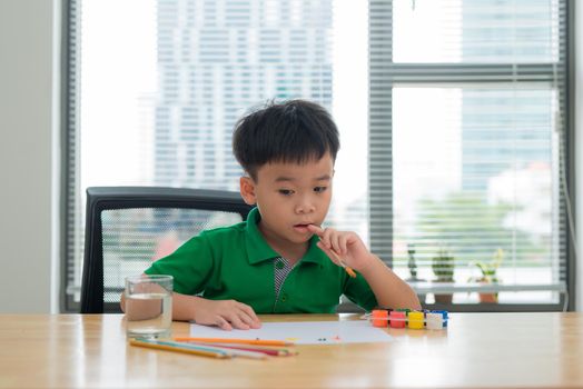 Kids at study table thinking.Kid holding a pen and a notebook with thinking face action.Boy doing homework at study table with thinking act.