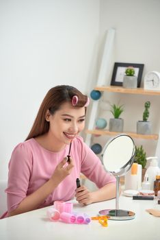 Serious attractive applying lip gloss and holding mirror in bright living room