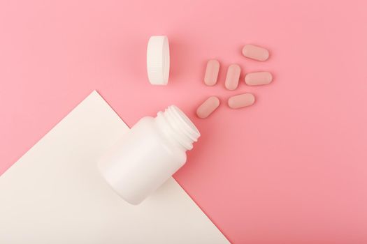 Creative flat lay with nutritional supplement or vitamins for woman. Opened medication bottle on pink background