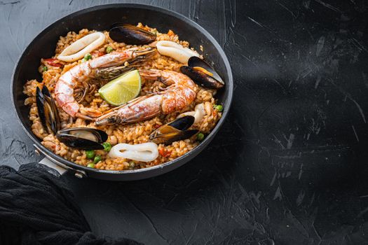 Valenciana paella with king prawns, mussels and squid on black background with copy space
