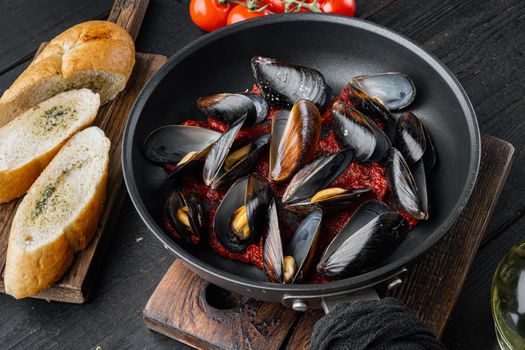 Mussels grilled with tomatoe sauce, on frying iron pan, on black wooden table background